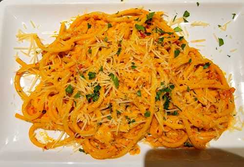 A plate of pasta topped with grated cheese and fresh herbs, served in a creamy orange sauce.