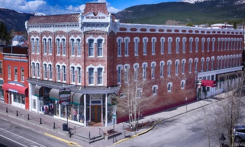 Historic brick building with multiple stories, shops on the ground floor, set against a mountain backdrop.