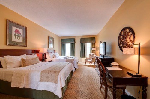 A cozy hotel room featuring two beds, a desk, a TV, and warm yellow walls with decorative art.