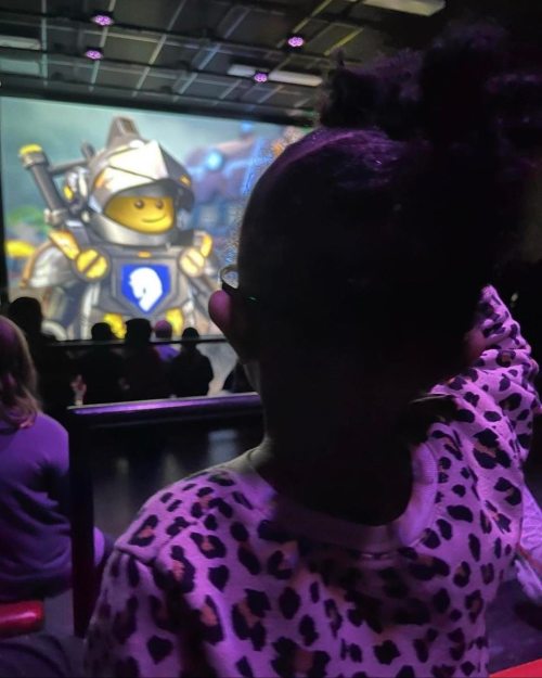 A child with curly hair watches a colorful animated projection in a dimly lit room.