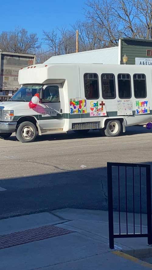 A decorated white bus with birthday signs and balloons parked on a street.