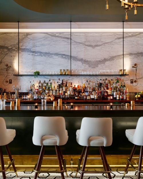 A stylish bar with a marble backdrop, featuring various bottles and elegant seating in a modern setting.