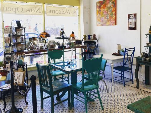 A cozy café interior with colorful chairs, tables, and decorative items, featuring large windows and a welcoming atmosphere.