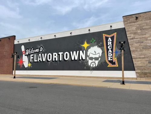 Mural on a building reading "Welcome to Flavortown" with a stylized graphic of a man and "Arcade" sign.