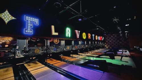 A vibrant bowling alley with colorful neon lights spelling "FLAVOR" and illuminated lanes in a dark setting.
