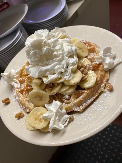 A plate of waffles topped with sliced bananas, whipped cream, walnuts, and powdered sugar.
