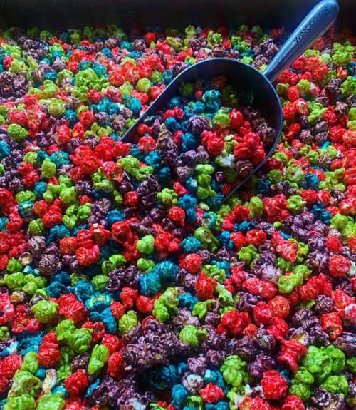 A colorful mix of popcorn in vibrant shades of red, green, blue, and purple, with a scoop resting on top.