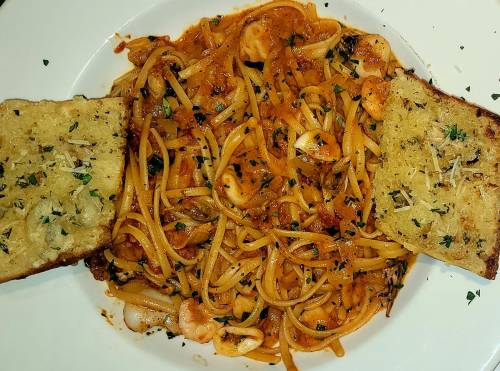 A plate of spaghetti with seafood in marinara sauce, garnished with parsley, accompanied by two slices of garlic bread.
