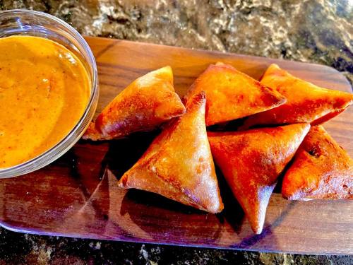 A wooden platter with golden-brown samosas and a small bowl of dipping sauce.