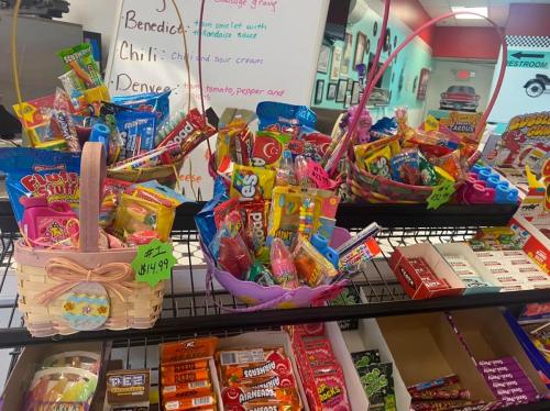Colorful baskets filled with assorted candies and snacks, displayed on a shelf in a store. Price tags visible.