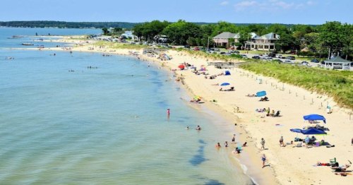 A sunny beach scene with people swimming, sunbathing, and colorful umbrellas lining the shore.