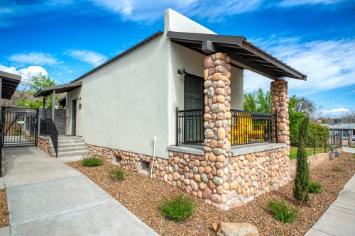 A modern house with a stone facade, covered porch, and landscaped yard under a blue sky.