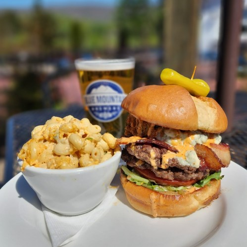 A juicy burger with bacon, lettuce, and sauce, served with a side of macaroni salad and a beer in the background.