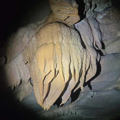 A close-up of a textured, stalactite-like formation in a dark cave, illuminated by a faint light.
