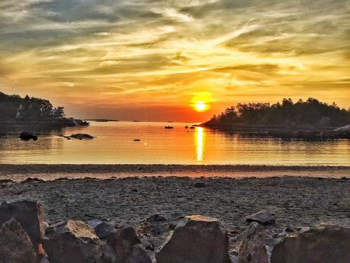 A serene beach at sunset, with golden hues reflecting on calm water and silhouettes of distant islands.