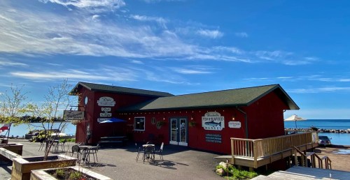 A red seafood market building by the water, with outdoor seating and a clear blue sky above.