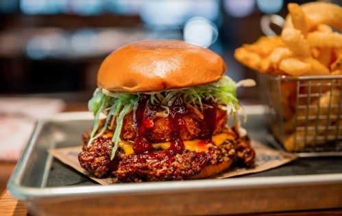 A close-up of a crispy chicken sandwich topped with lettuce, cheese, and sauce, served with a side of fries.