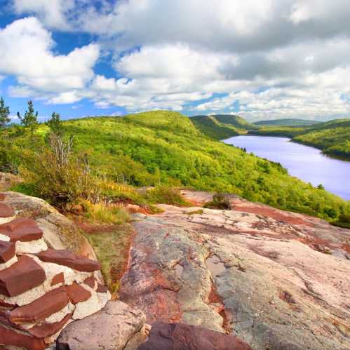 A scenic view of lush green hills and a winding river under a bright blue sky with fluffy white clouds.