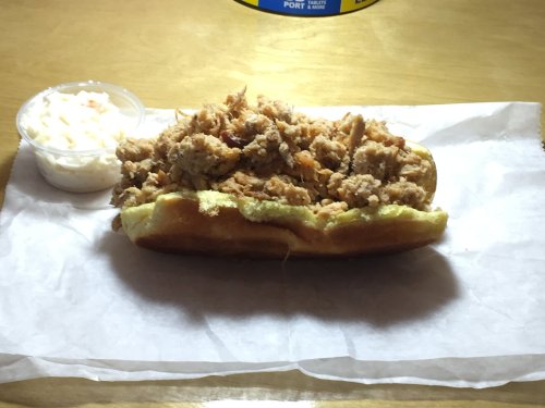 A hot dog bun filled with shredded fried chicken, served with a side of coleslaw in a small cup.