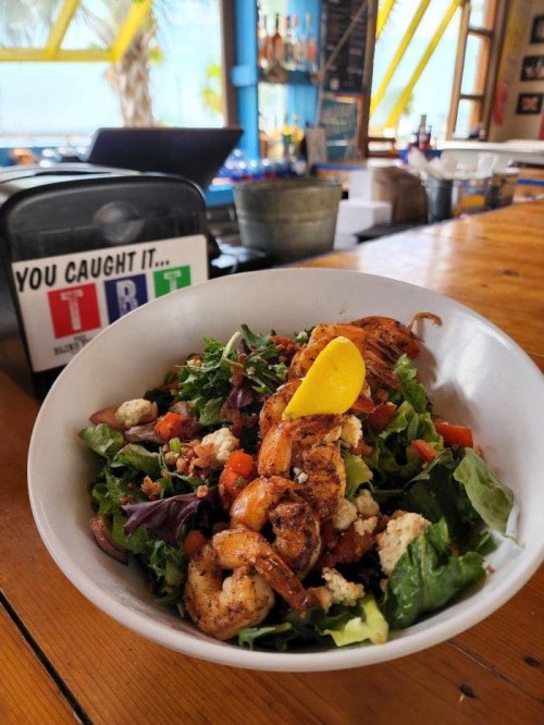 A vibrant salad with grilled shrimp, mixed greens, tomatoes, and feta cheese, served in a bowl on a wooden table.