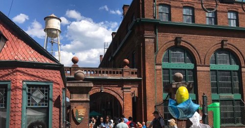 A bustling outdoor scene featuring a historic brick building, a water tower, and people enjoying the day.