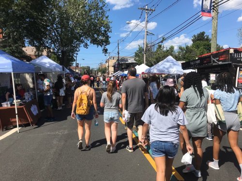 A busy street fair with people walking among vendor tents under a clear blue sky.