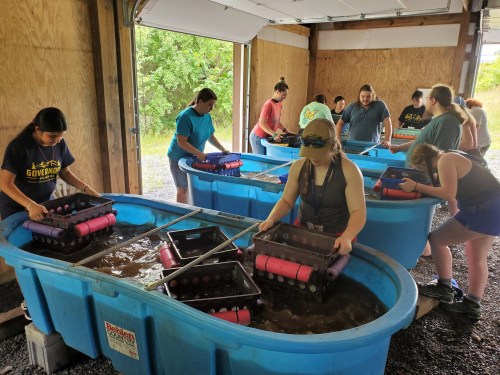 A group of people working in a garage, using large blue tubs filled with water and equipment for an activity.