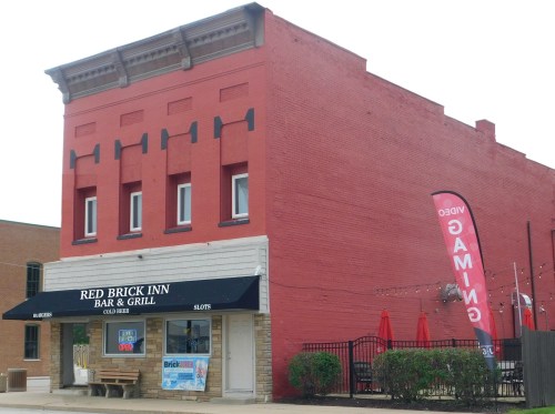 Exterior of the Red Brick Inn Bar & Grill, featuring a red brick building, outdoor seating, and a gaming banner.
