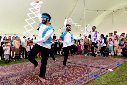 Three dancers perform under a tent, showcasing colorful costumes and energetic movements, with an audience watching.