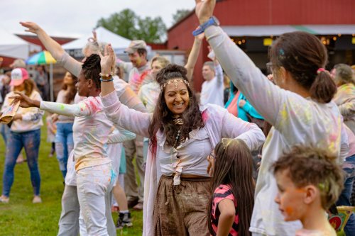 A joyful crowd celebrates at a colorful outdoor festival, dancing and covered in vibrant powders.