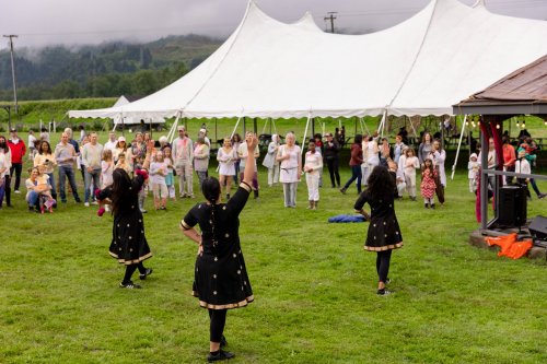 Three dancers in traditional attire perform in front of a crowd under a large tent on a grassy field.