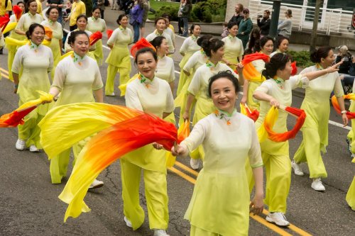 A group of women in yellow outfits perform a dance with colorful ribbons during a parade.
