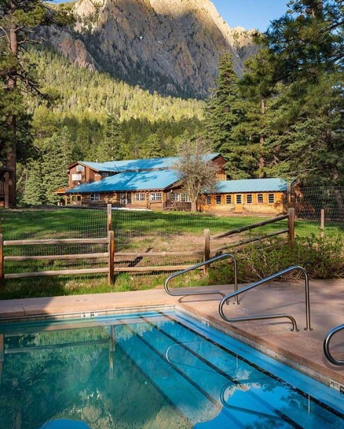 A serene lodge surrounded by trees and mountains, with a swimming pool in the foreground.