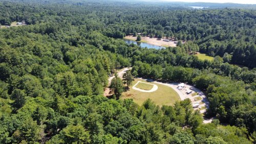 Aerial view of a lush green forest with a small pond and a clearing for activities in the center.