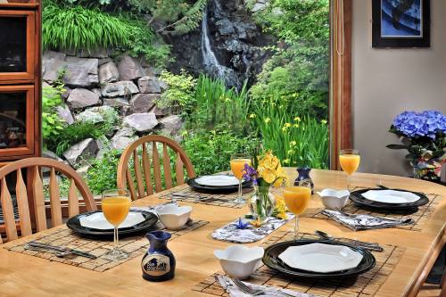 A beautifully set dining table with orange drinks, flowers, and a scenic view of a garden and waterfall outside.