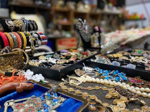 A variety of colorful jewelry displayed on tables, including necklaces, bracelets, and rings in a market setting.