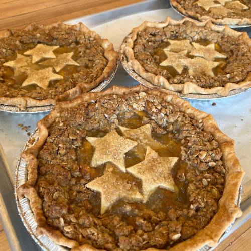 Four freshly baked pies with star-shaped crusts on a baking tray, featuring a golden filling and crumbly topping.