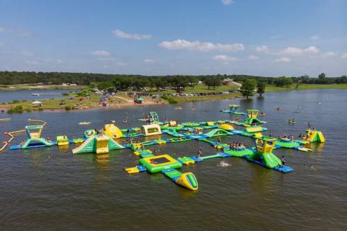 Aerial view of a colorful inflatable water park on a lake, with people enjoying various attractions and activities.