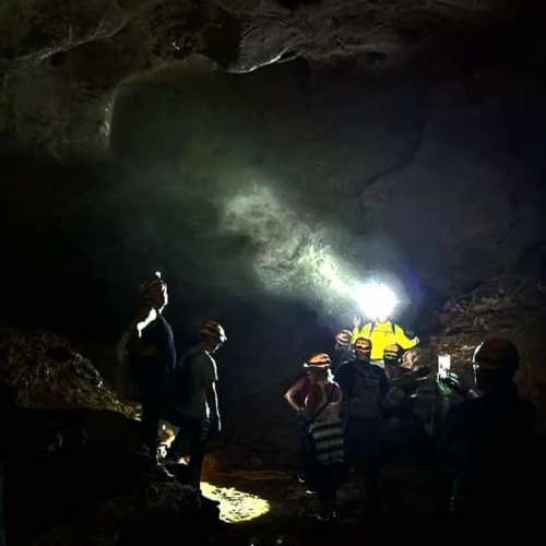 A group of people exploring a dark cave, illuminated by flashlights, with rocky walls and a mysterious atmosphere.