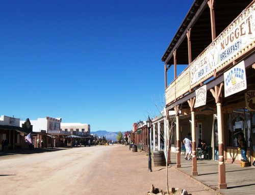 A wide view of a historic western town street with wooden buildings and clear blue skies.
