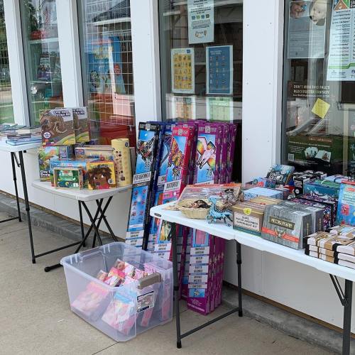A display of various toys and games on tables outside a store, with colorful packaging and a clear plastic bin.