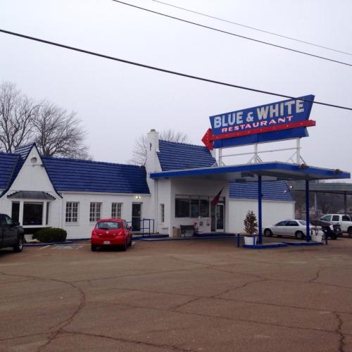A white restaurant building with a blue roof and a sign reading "Blue & White Restaurant" in a suburban setting.