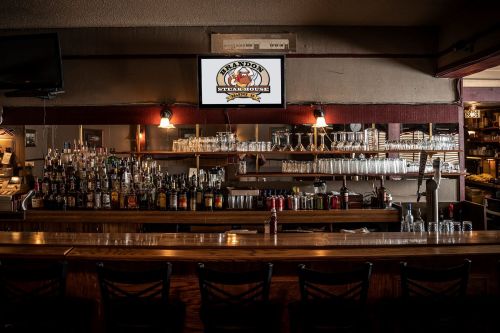 A cozy bar with a wooden counter, shelves of liquor, and a TV displaying the restaurant's logo.