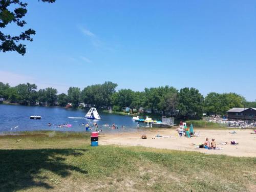 A sunny beach scene with people swimming, a water slide, and green trees surrounding a calm lake.
