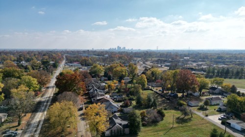 Aerial view of a suburban area with colorful autumn trees and a distant city skyline under a partly cloudy sky.