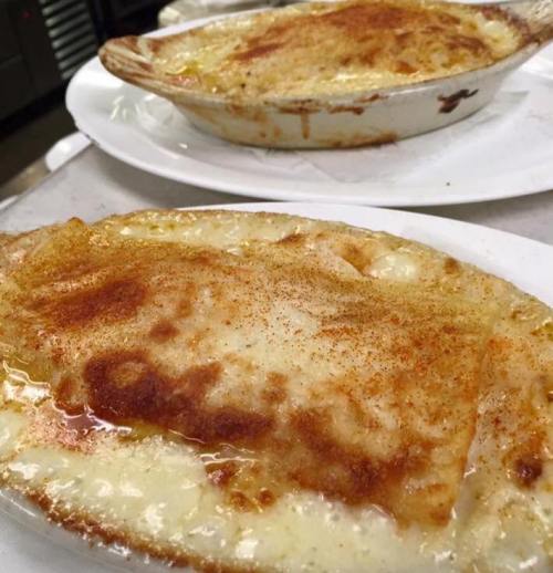 Two baked dishes with creamy, golden cheese topping and a sprinkle of seasoning, served on white plates.