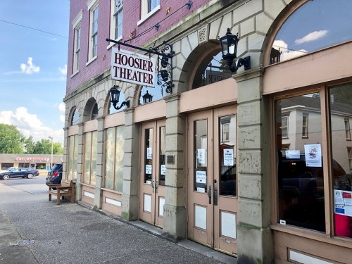 Exterior of the Hoosier Theater, featuring large windows, a sign, and decorative light fixtures.