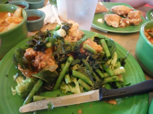 A plate of fried food on a bed of mixed greens and broccoli, with a knife resting beside it.