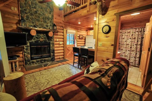 Cozy log cabin interior with a stone fireplace, wooden walls, and a rustic decor. A warm, inviting atmosphere.