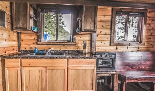Cozy wooden kitchen with a sink, stove, and natural light from windows, featuring rustic decor and a warm atmosphere.